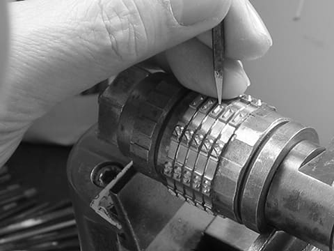 A picture of a craftsman grinding a number by hand on a press and roll marking machine.