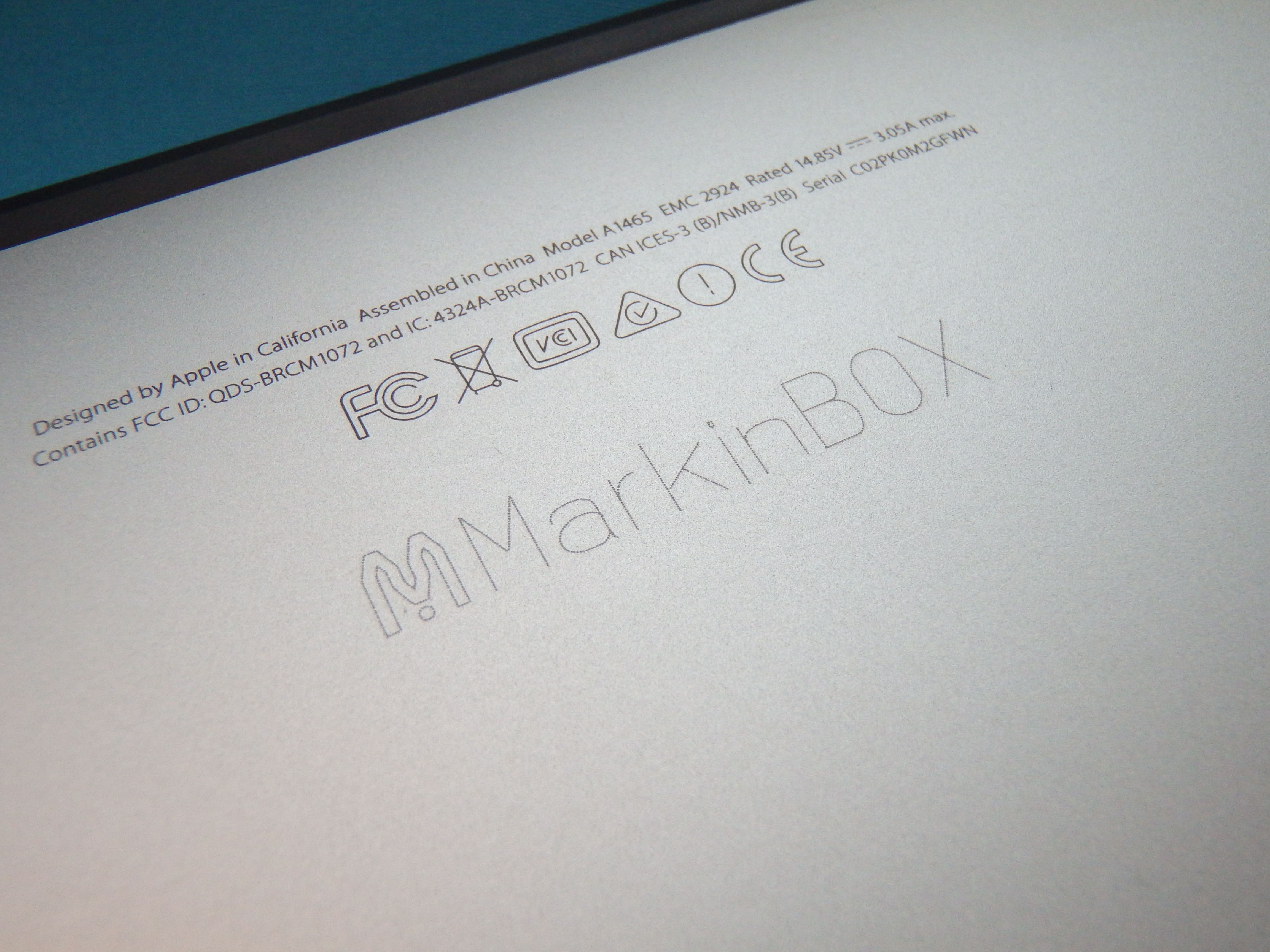 Image of the Computer's Back panel engraved with 'MarkinBOX' and logo, and text that reads 'Designed by Apple in California Assembled in China Model A 1465 EMC 2924 Rated 14.85V 3.05A max. Contains FCC ID: QDS-BRCM1072 and IC: 4324A-BRCM1072 CAN ICES-3 (B)/NMB-3(B) Serial C02PK0M2GFWN'