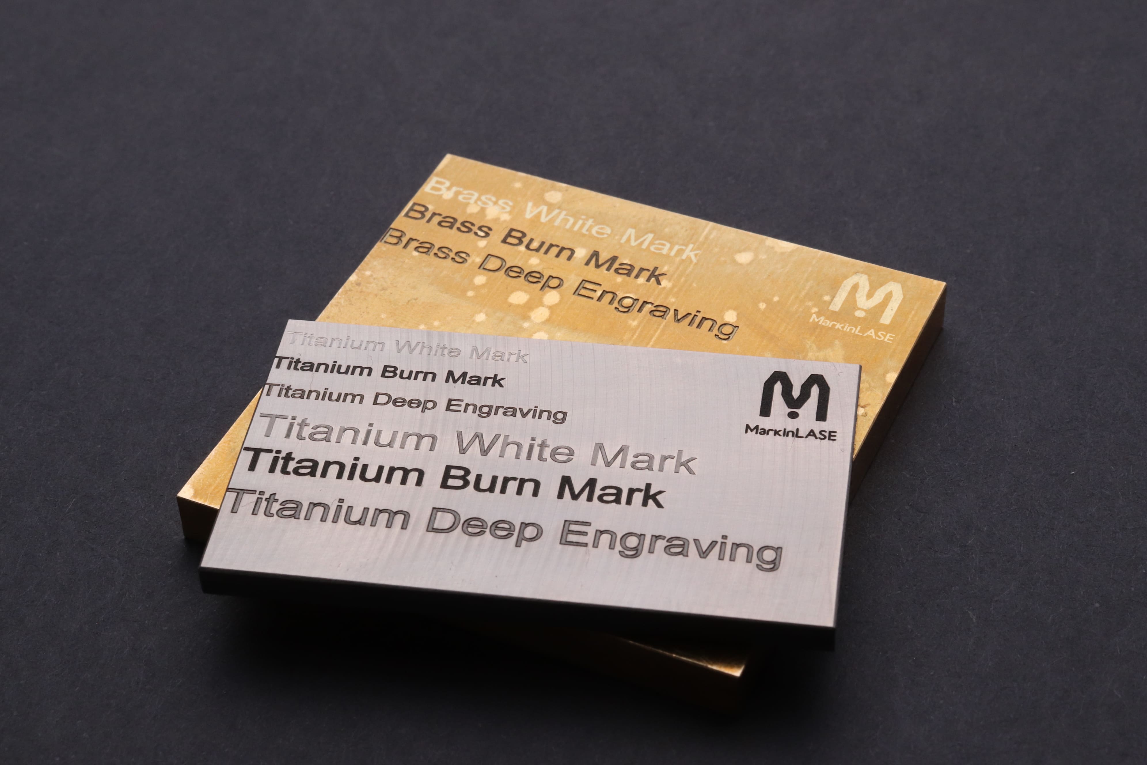 Image of 2 thick plates of titanium and brass materials with MarkinLase logo for all and 'Titanium White Mark, Titanium Burn Mark, Titanium Deep Engraving and Brass White Mark', 'Brass Burn Mark, Brass Deep Engraving' for each.