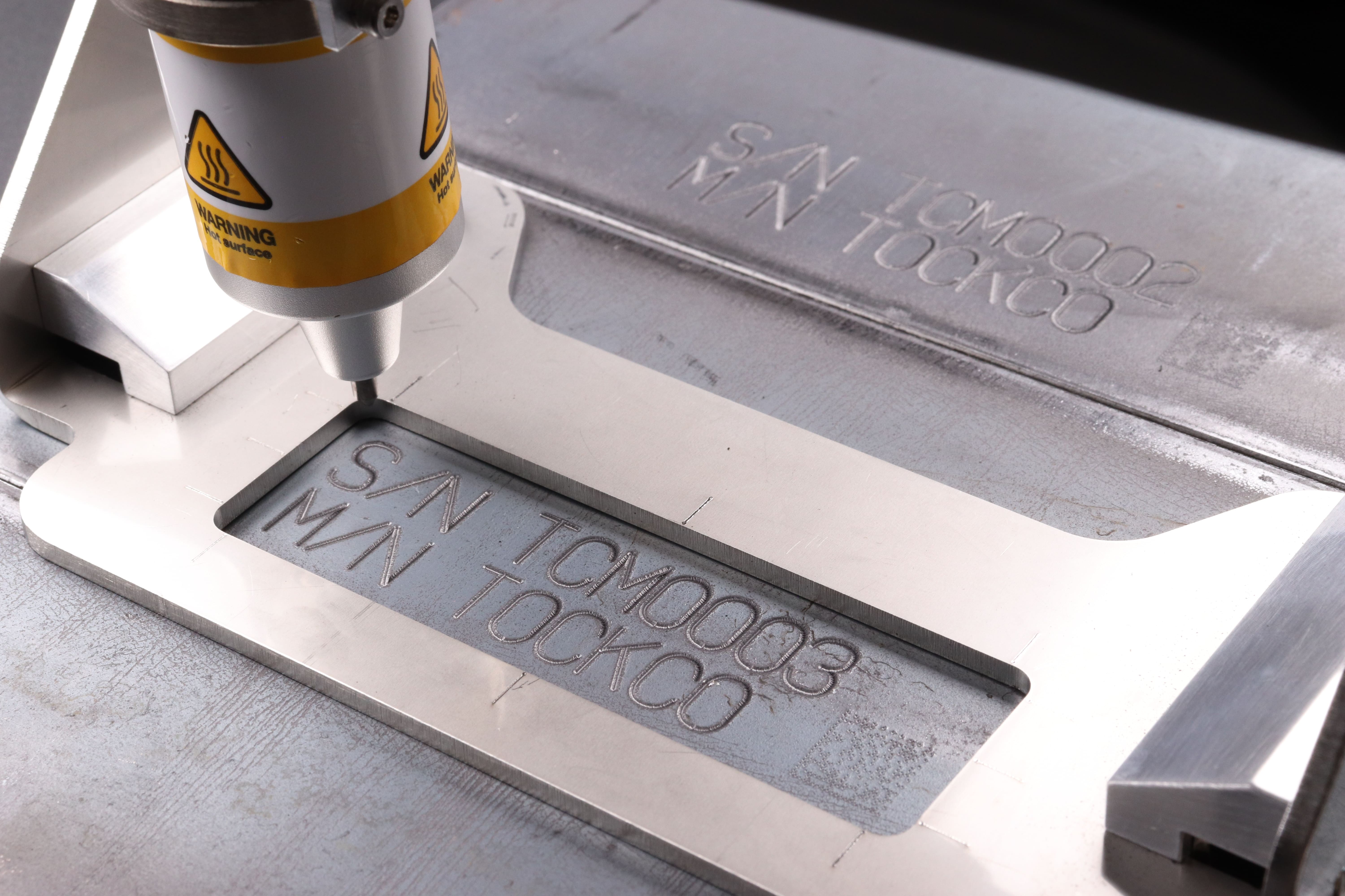 Image of metal steel material engraved with text and numbers 'S/N TCM0003 M/N TOCKCO'.