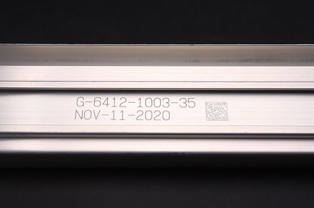Close-up of a piece of metal with a QR code and numbers engraved on it.It contains the text 'G-6412-1003-35 NOV-11-2020'. 